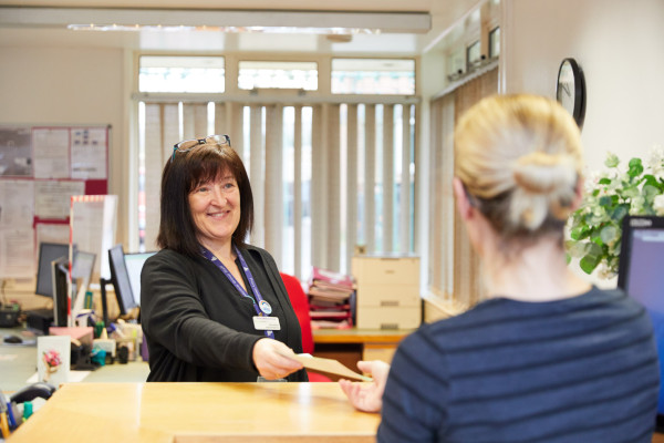 A photo showing a Rawcliffe receptionist handing a patient a prescription